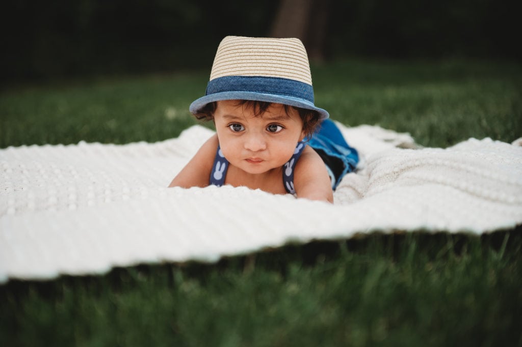Newborn Photographer, a baby boy lays ona blanket in the grass with a hat on his head