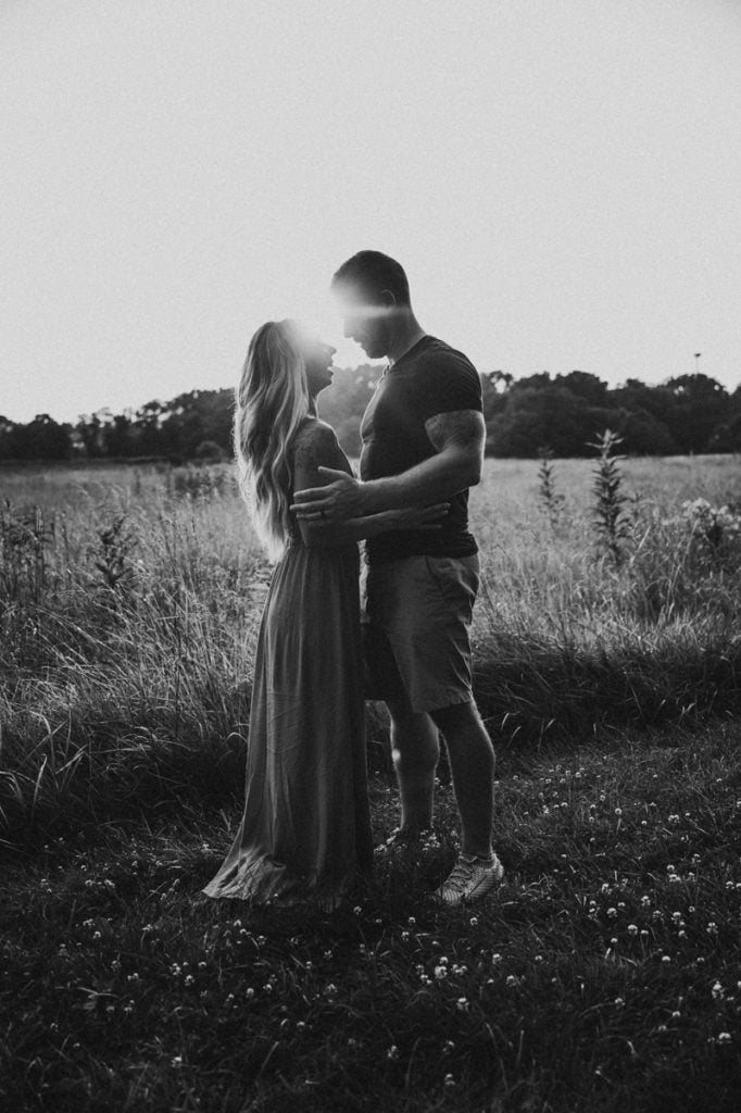 Family Photographer, a young man and woman embrace in a field, they are happy